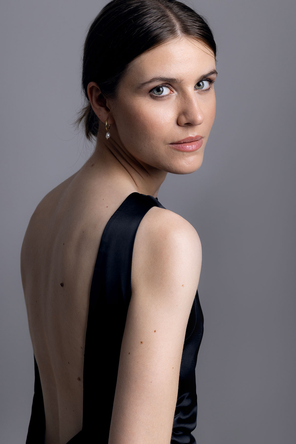 Retrato feminino editorial em estúdio com vestido preto de costas abertas e expressão elegante, fotografado por Danniela Senra em Castelo Branco
