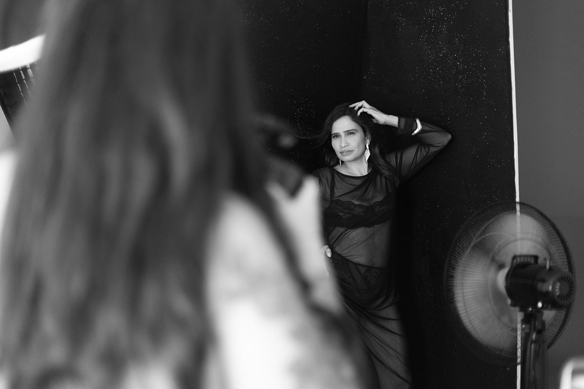 bastidores de uma mulher sendo fotografada em um fundo preto e com a mão na cabeça