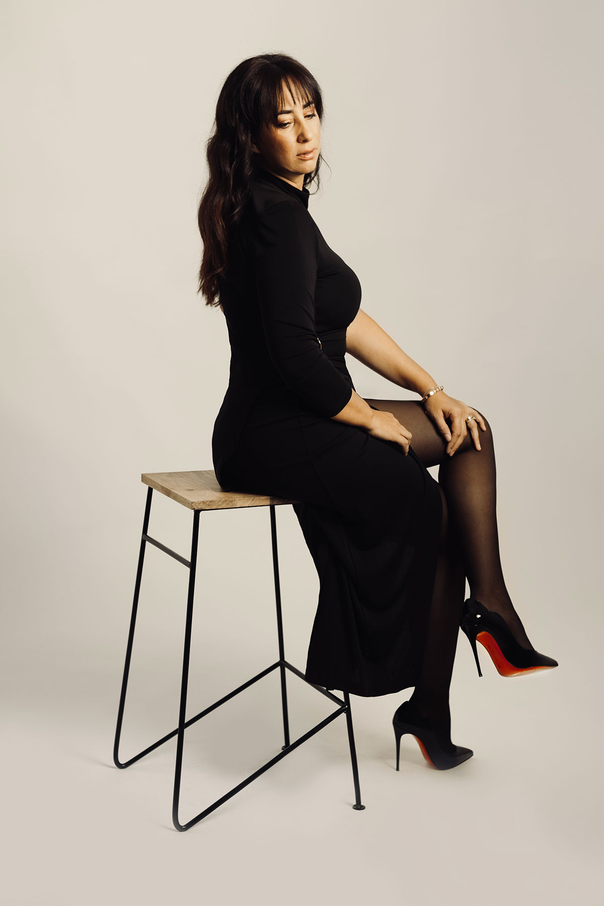 retrato em estúdio mulher vestida de preto sentada num banco com sapatos louboutin