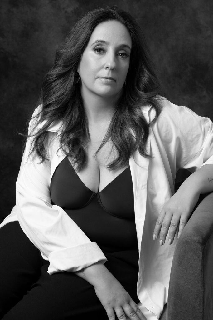 Retrato feminino editorial em estúdio, em preto e branco, com camisa branca aberta e expressão confiante
