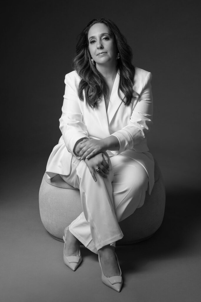 Retrato feminino editorial em estúdio, em preto e branco, com fato branco e pose sentada