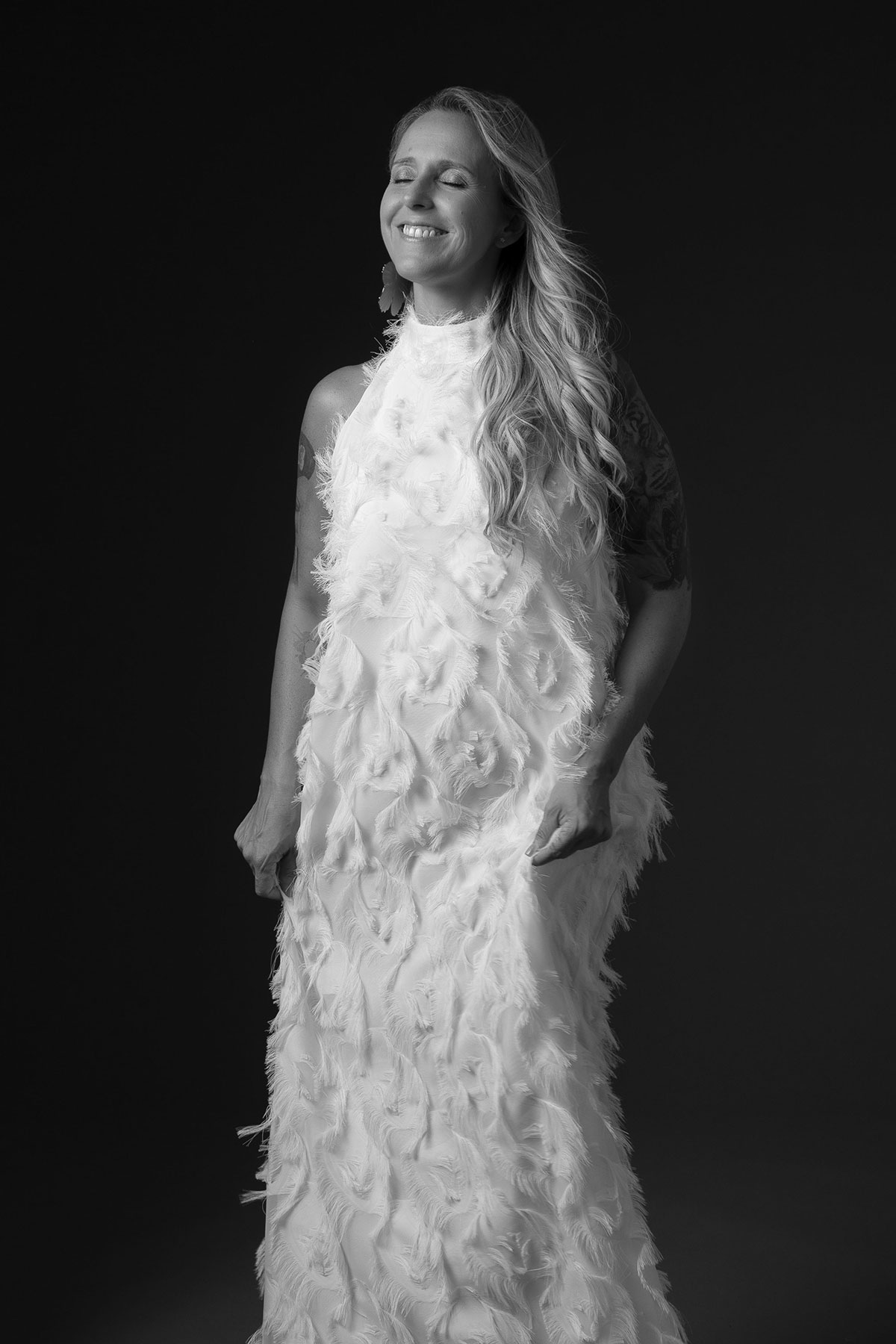 Retrato feminino editorial em estúdio com vestido de plumas branco e expressão natural.